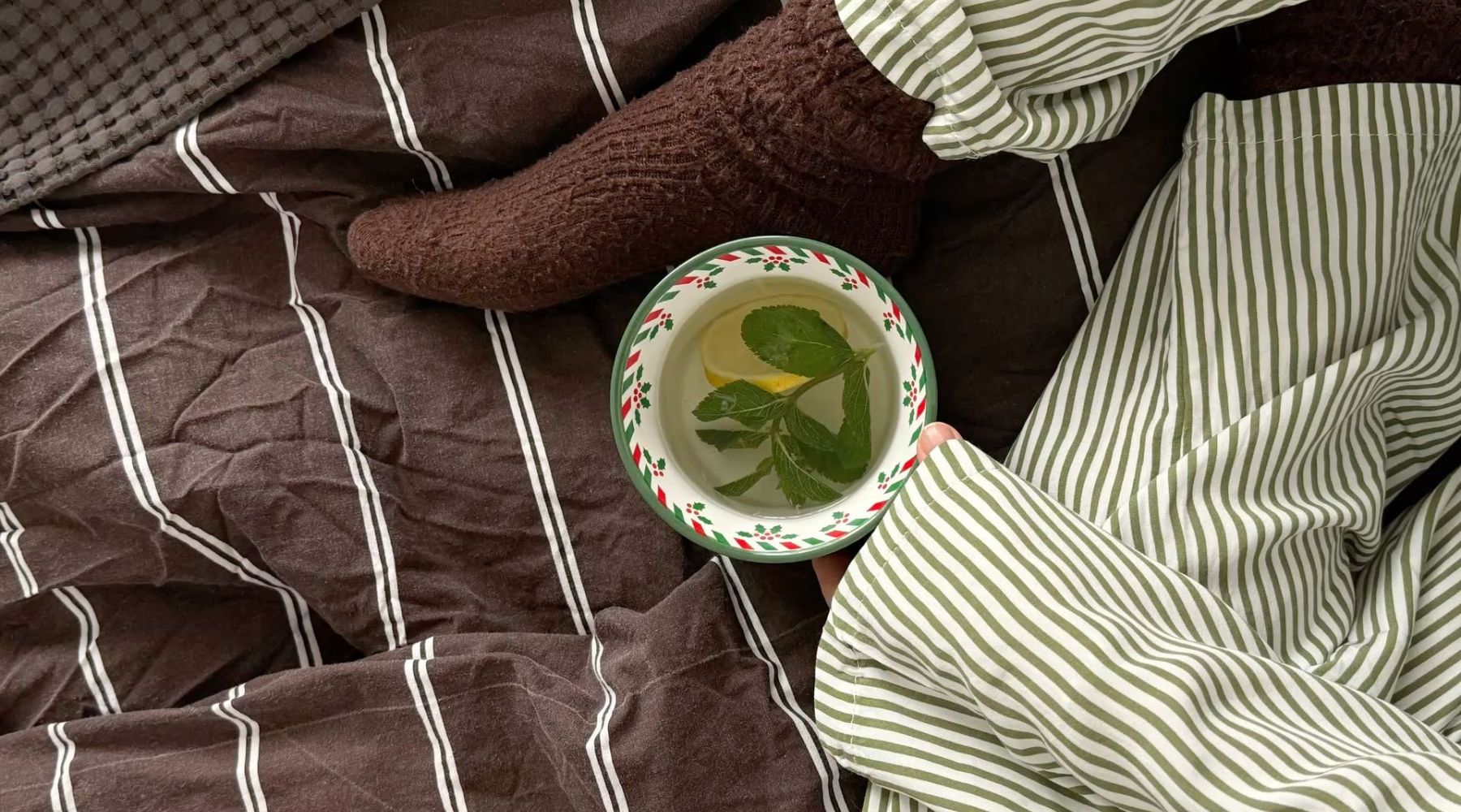 Ambiance cozy avec une bougie Cachemire + Thé vert allumée, tasse de thé chaud et couverture douce.