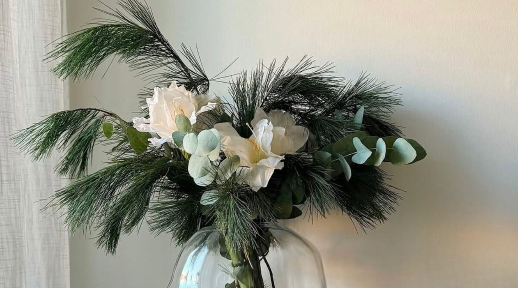 Bouquet d’hiver composé de branches de sapin, de fleurs blanches et de feuillages pâles, présenté dans un vase pour accompagner la fragrance Sapin + Fleur de cactus.